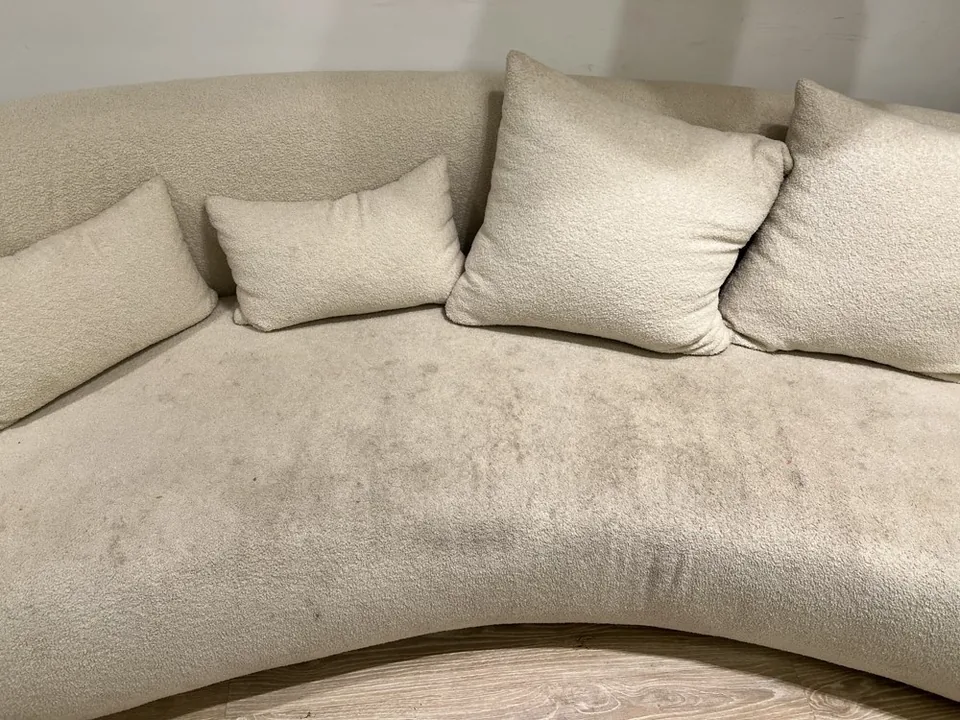 Curved cream sofa before cleaning, with visible marks across the seat